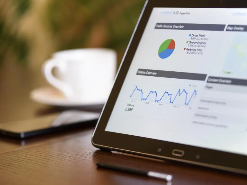 Tablet showing traffic and pipeline dashboards beside a coffee cup on dark wood
